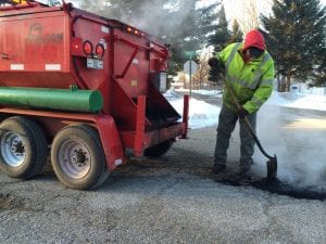 A Falcon worker spreads hot mix asphalt over a pothole.