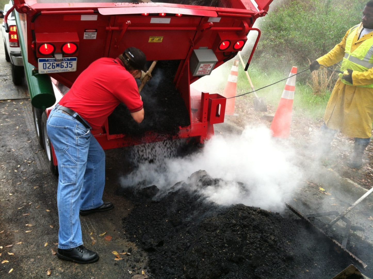 A worker shoveling hot mix asphalt from a hot box into a pothole for repair.