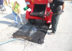 a road repair crew repairs potholes with an asphalt hot box