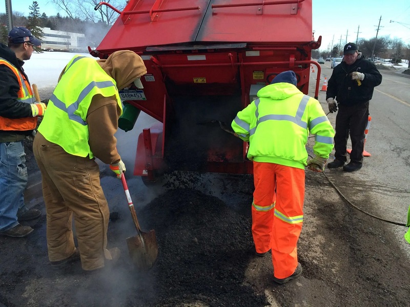 Workers using a Falcon asphalt hot box pothole repair machine to fill a hole.
