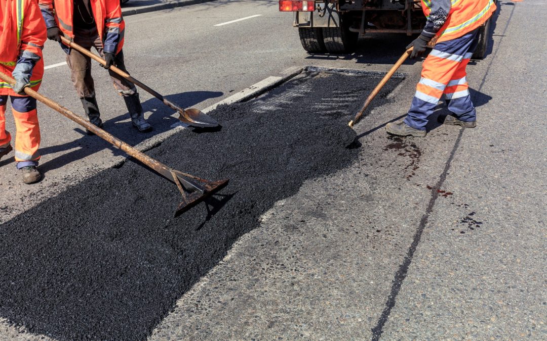 Municipal road maintenance crews perform pothole repairs using shovels to evenly distribute asphalt.