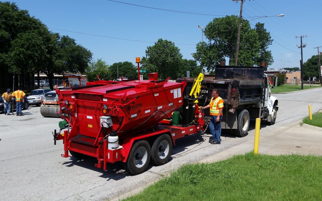 A municipal maintenance worker using a red Falcon Asphalt Hotbox to patch potholes.